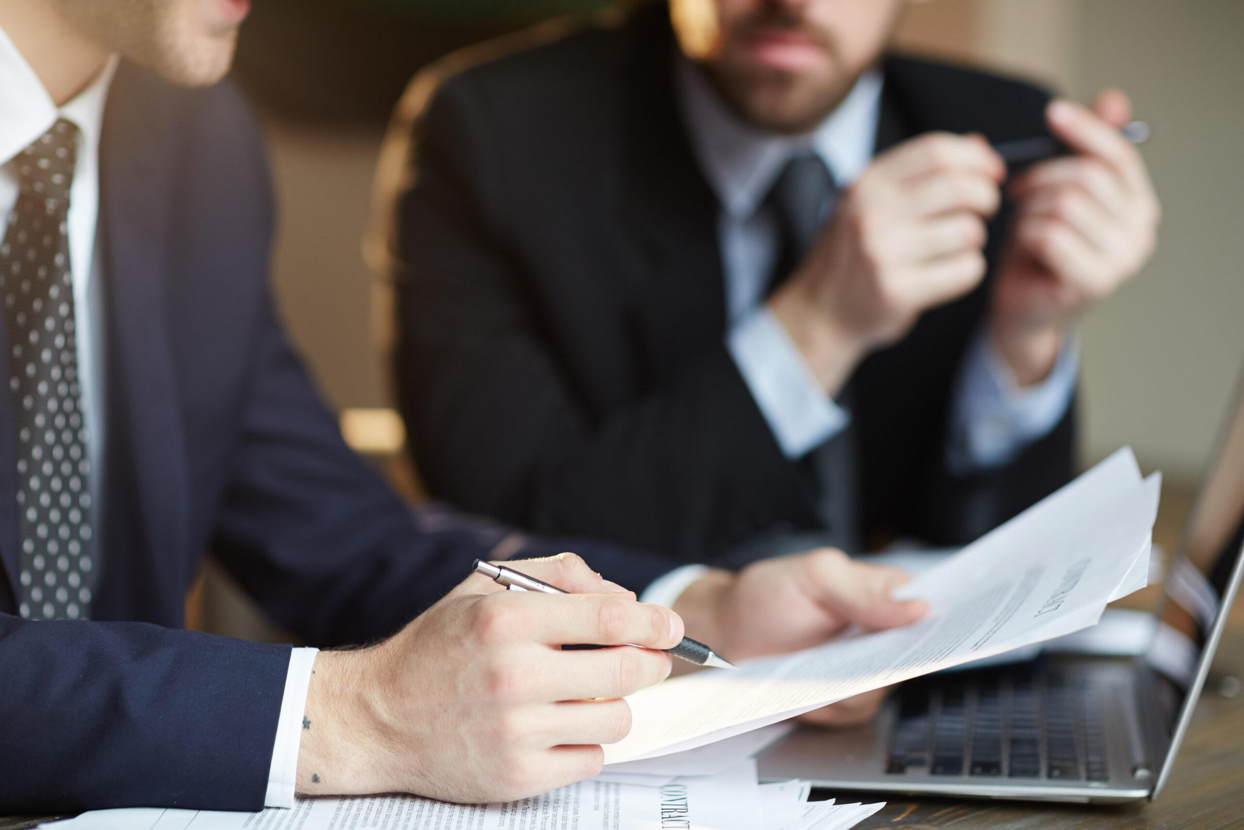 Closeup portrait of two unrecognizable business partners reviewing paperwork and signing contract papers at table during meeting